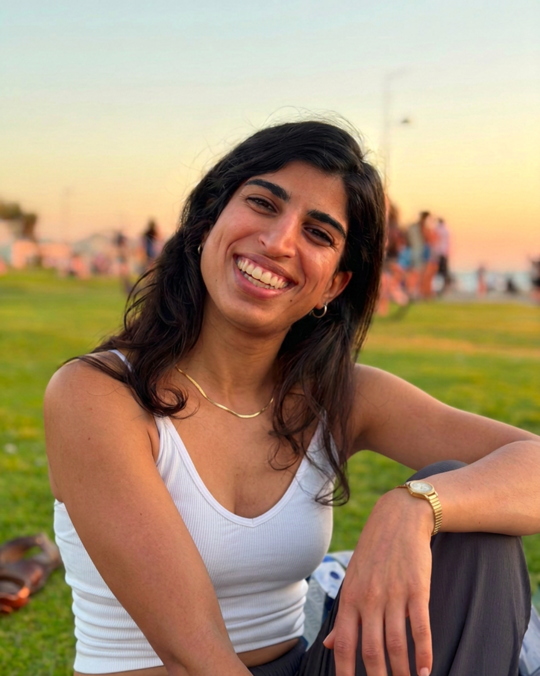 סהר מחייכת בישיבה על הדשא בשקיעה